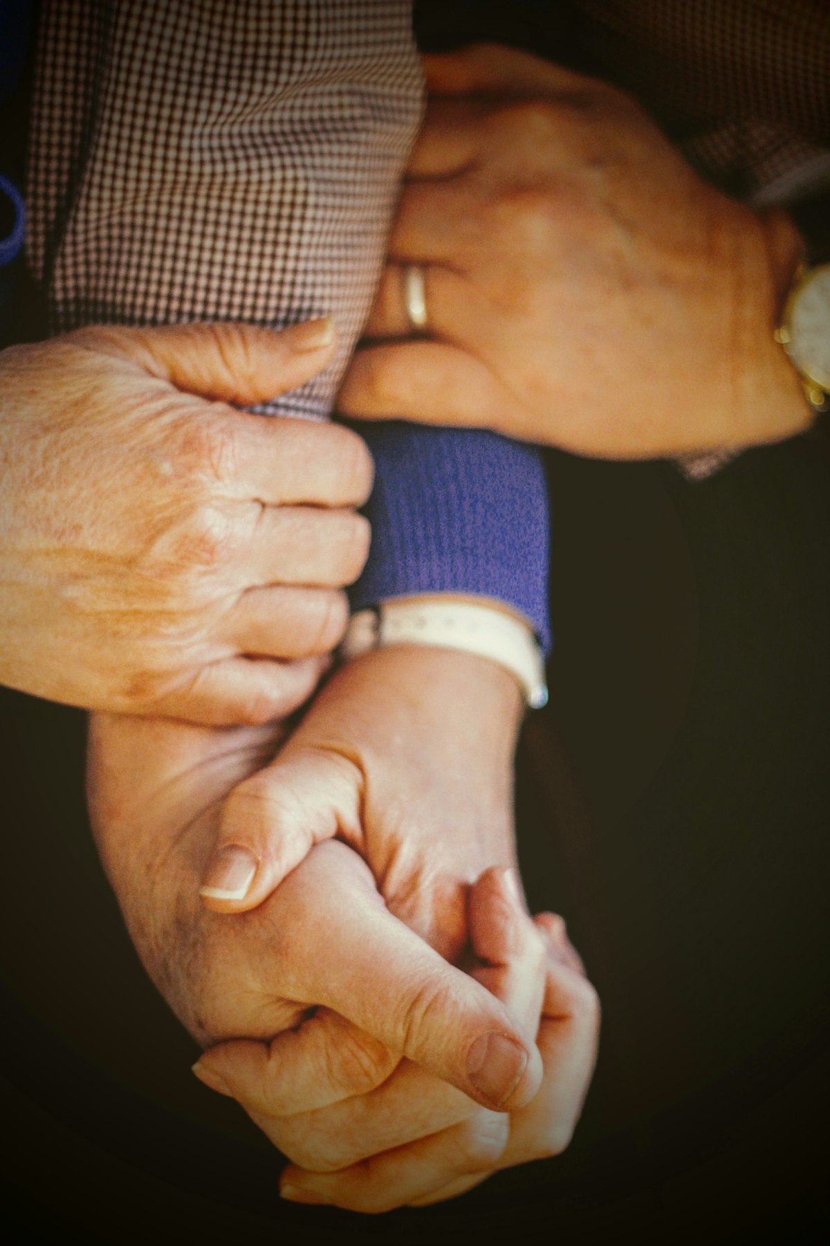 A younger hand gently holding an older adult’s hands