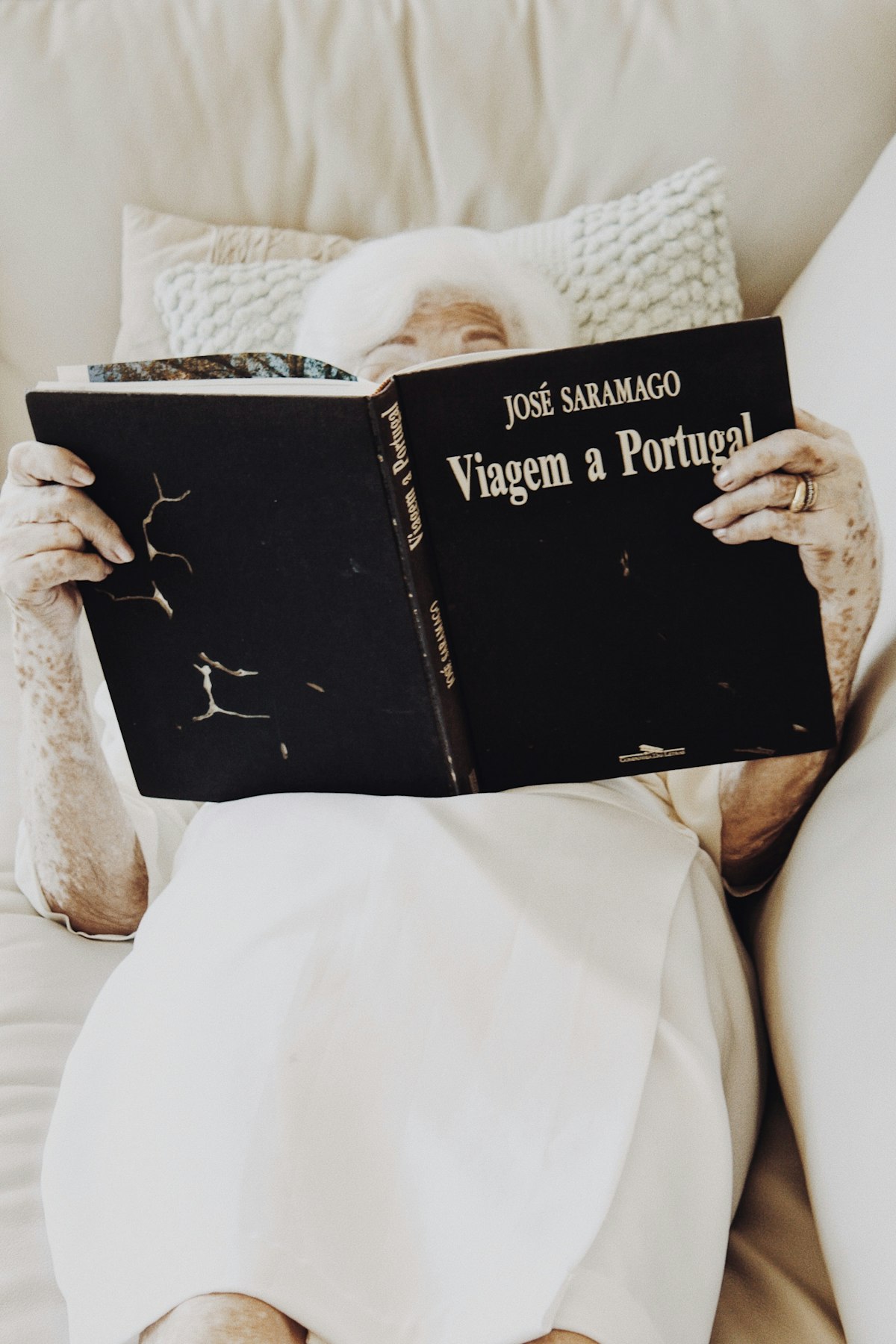 An older woman relaxing on a sofa reading a book